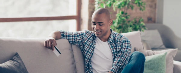 A man sitting on his couch looking at his credit card.
