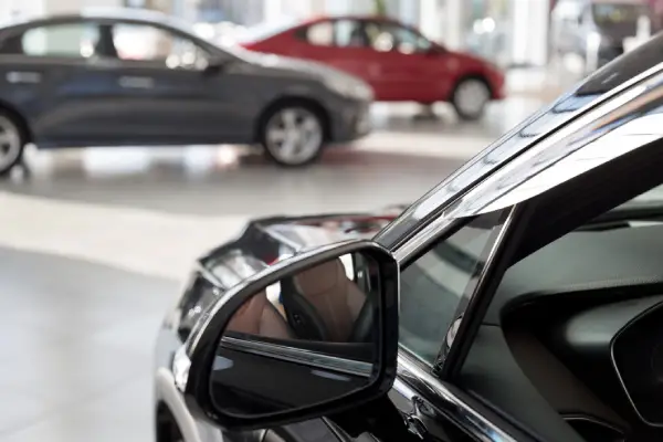 A black vehicle sits across from other cars at a dealership.