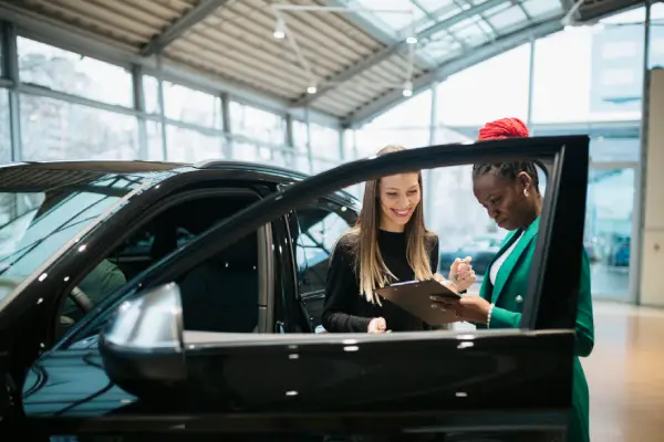 A woman signs paperwork next to her new car.