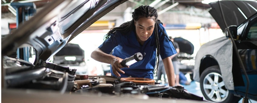 Car mechanic leans over opened car hood to work on vehicle.