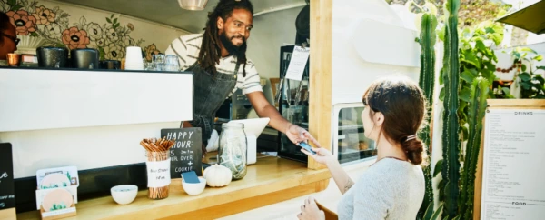 A man in a food truck hands a credit card back to female patron.