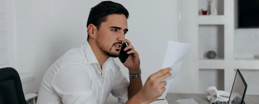 man looking at piece of paper while on the phone