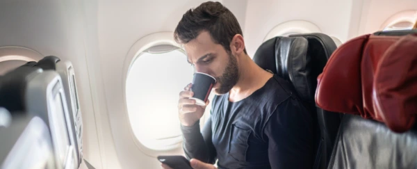 A man sipping from a cup while sitting on an airplane.